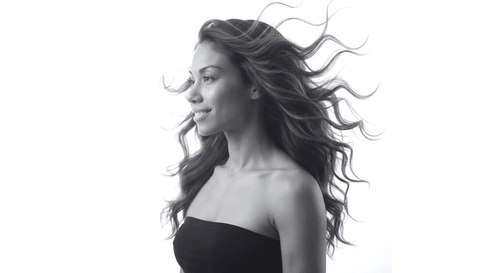 A grayscale landscape image of a woman in profile wearing a black tube top, with her long, wavy hair blowing in the wind.